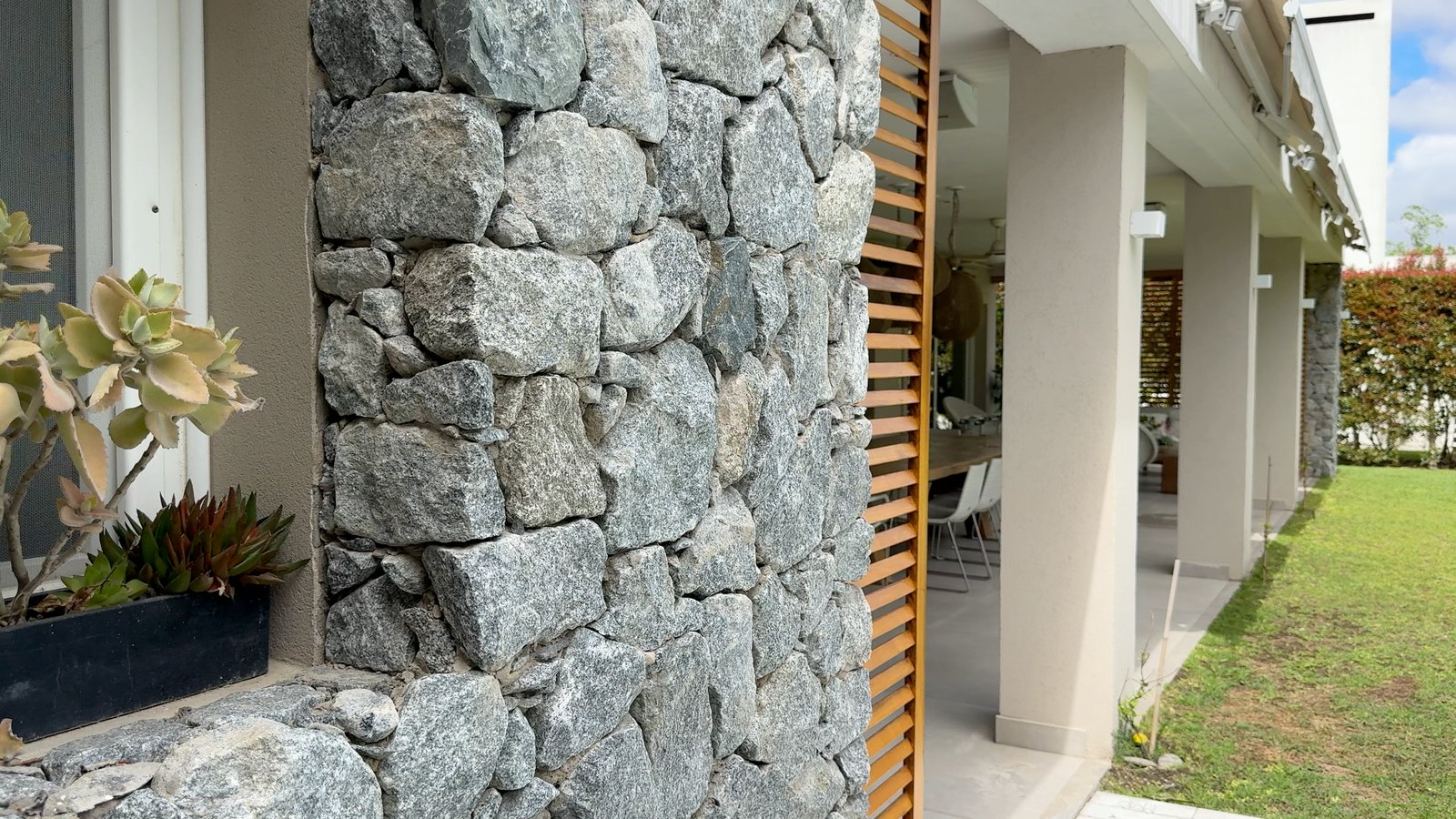 Detalle de muro de piedra y fachada moderna con vegetación — proyecto CASA CM, por Hermann Arquitectos, en Los Castores